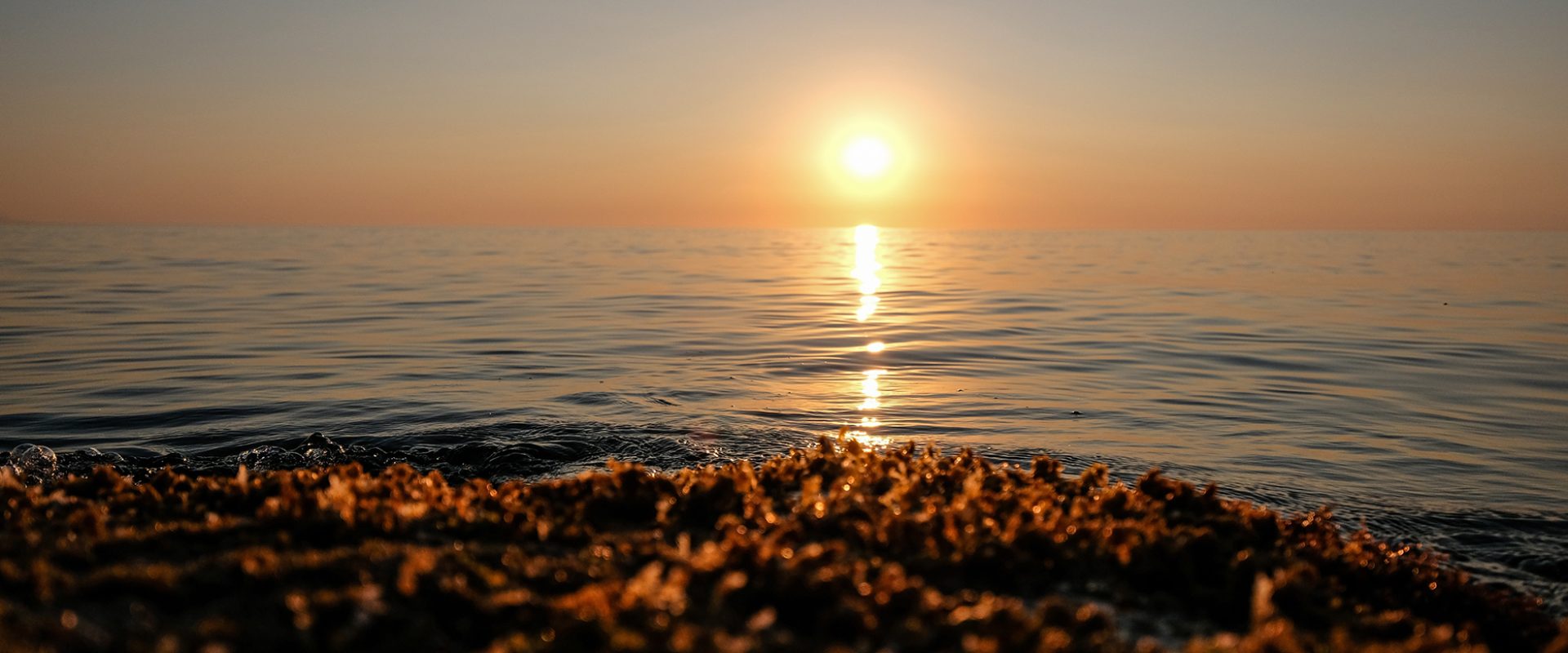 A beautiful shot of sea with waves and sun in a distance with clear sky at sunset